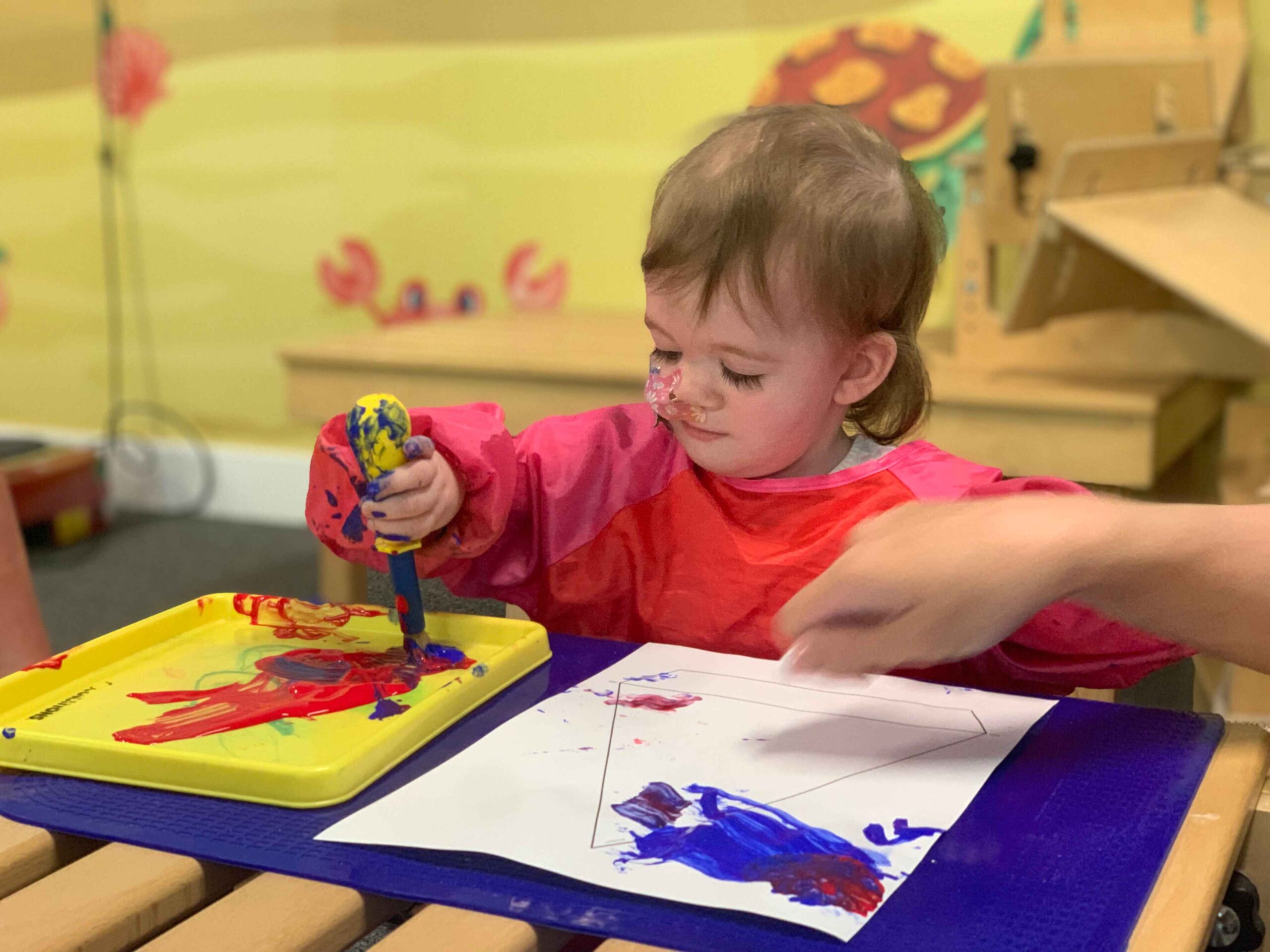 A young girl with a life limiting condition is playing with red and blue paint on paper.