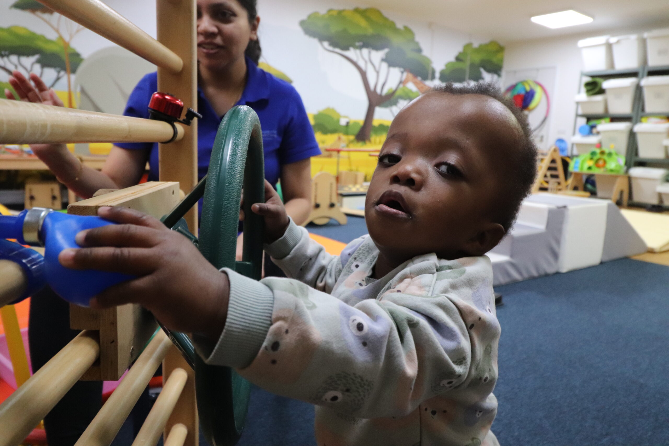 A young girl with Noonan syndrome plays with a driving toy while standing.