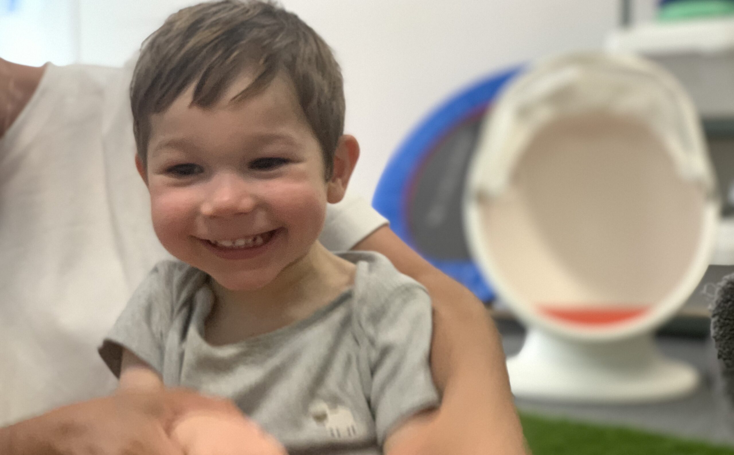 A young boy with Galloway- Mowat syndrome is being held to sit up and is smiling. He has short dark hair.